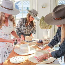 Three women decorating white felt hats with ribbons