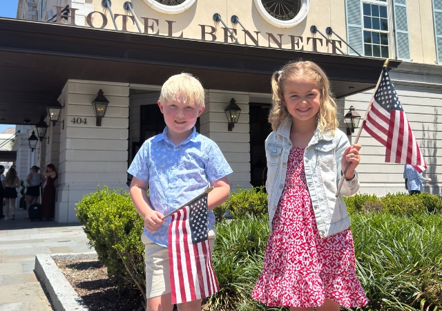 An image of a little boy holding an American flag in front of Hotel Bennett